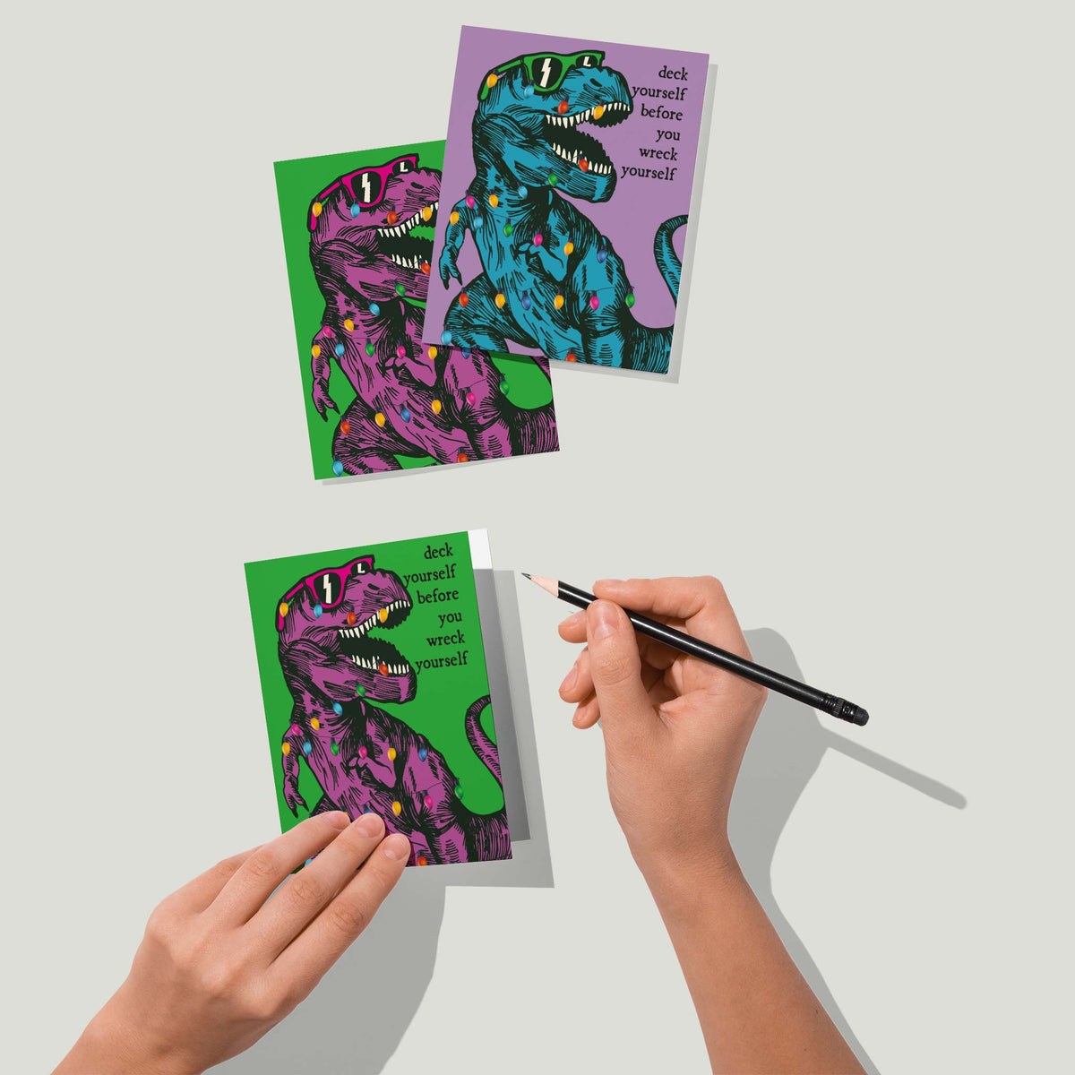 Holiday cards with right-aligned dark serif text beside a string-light-wrapped T-rex, set of 24.