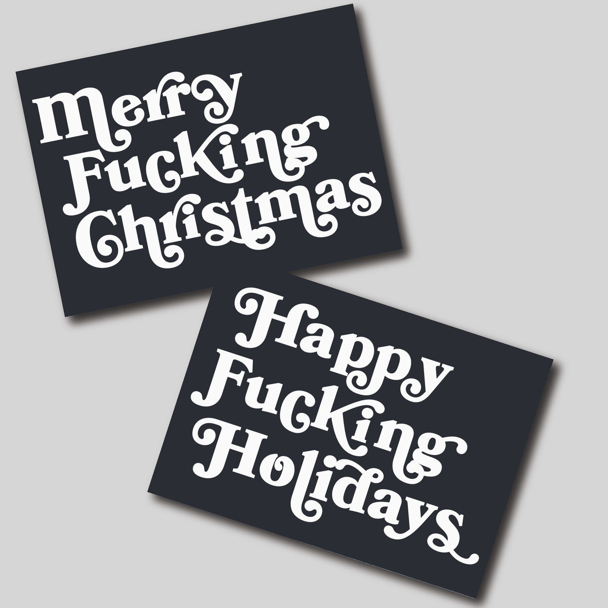 Card set featuring two expletive Christmas greeting designs in white 1970s swash serif lettering on charcoal.