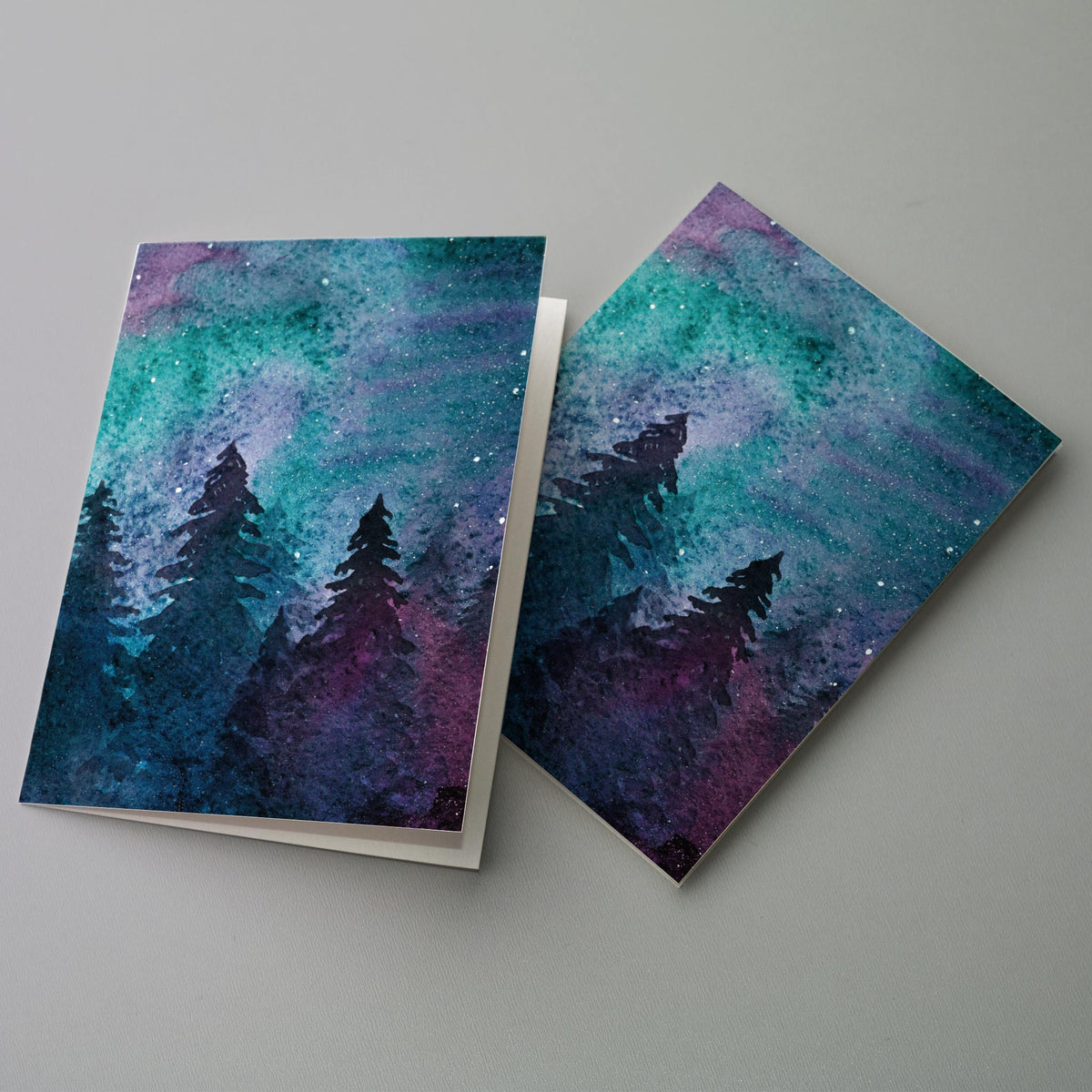 Set of 24 folded holiday cards, one design, watercolor-style sky in teal, turquoise, purple, and magenta with star-like dots.