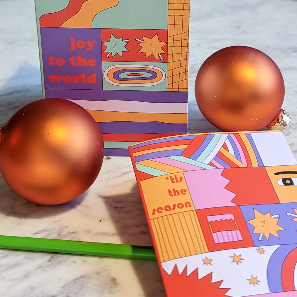 Four holiday card designs on lavender, orange, mint green, and maroon backgrounds with patchwork panel illustrations.