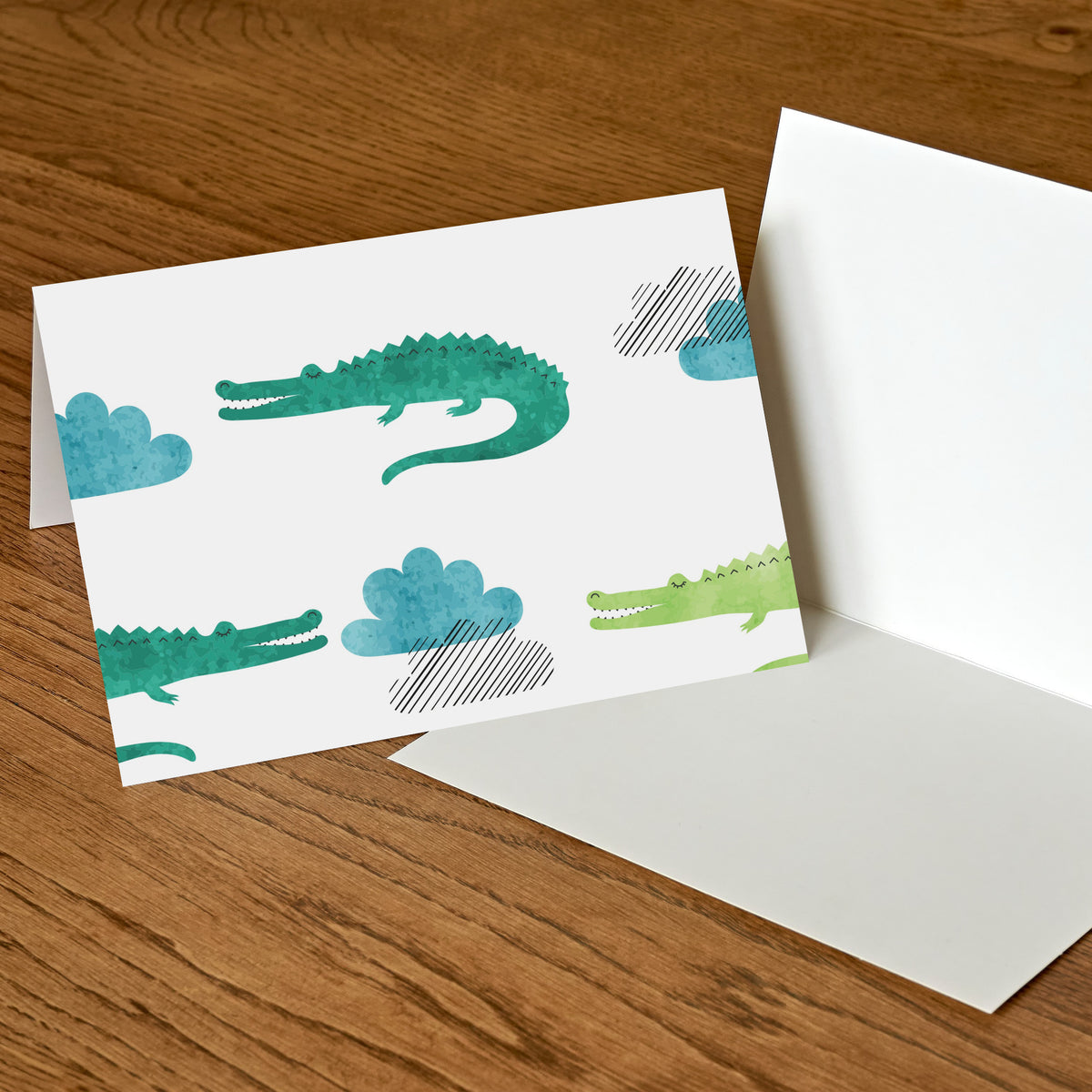 Two-design card set, 12 each: scattered watercolor-style crocodilians with blue and gray cloud shapes.