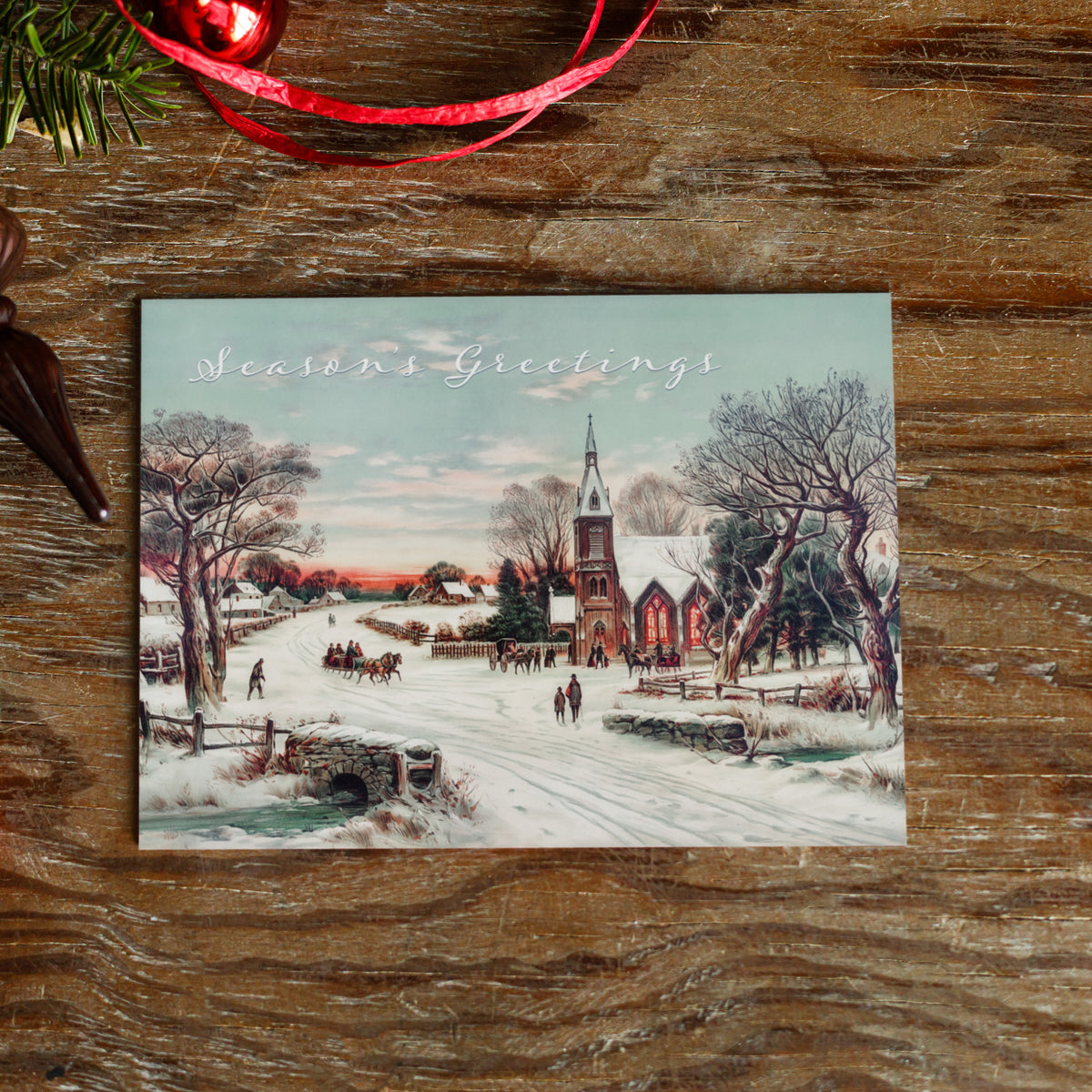 Christmas cards with a dusk winter landscape, stone arch bridge, bare trees, and red-lit arched church windows.
