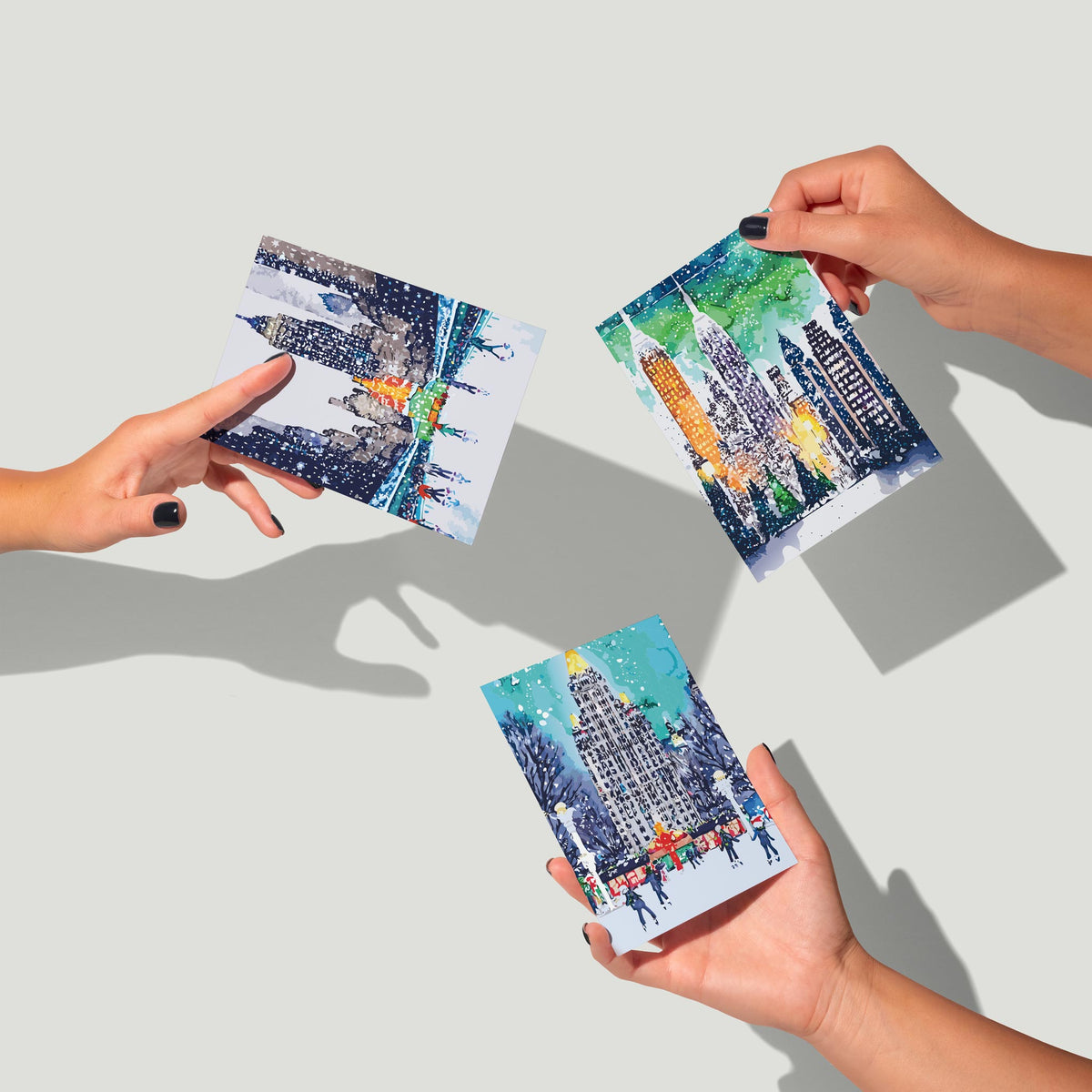 Six watercolor city scene designs showing snowy plazas, lit skyscrapers, and ice skaters in winter settings.