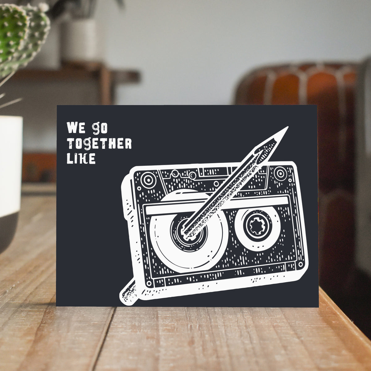 White cross-hatched cassette tape illustration on full-bleed black card with all-caps text reading "we go together like."