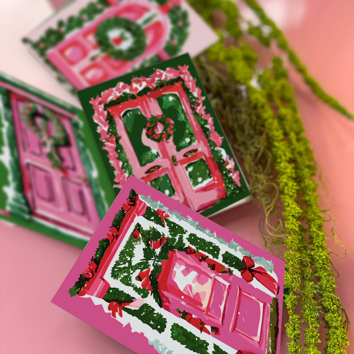 Christmas card set, four designs, each showing a decorated pink door with green wreaths, garland, and red accents.