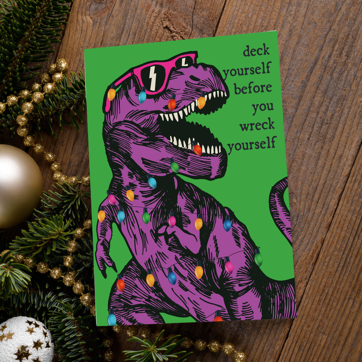 Set of 24 holiday cards featuring a roaring T-rex in sunglasses tangled in multicolor bulb lights.