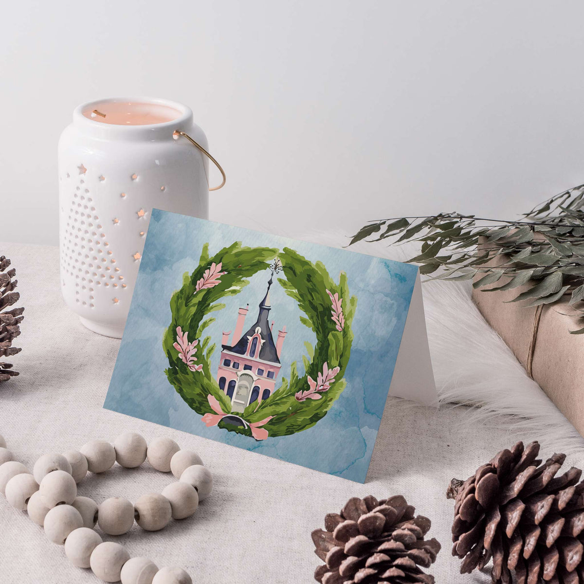 Watercolor-style Christmas cards depicting a pink mansion with a tall spire framed by a green wreath.