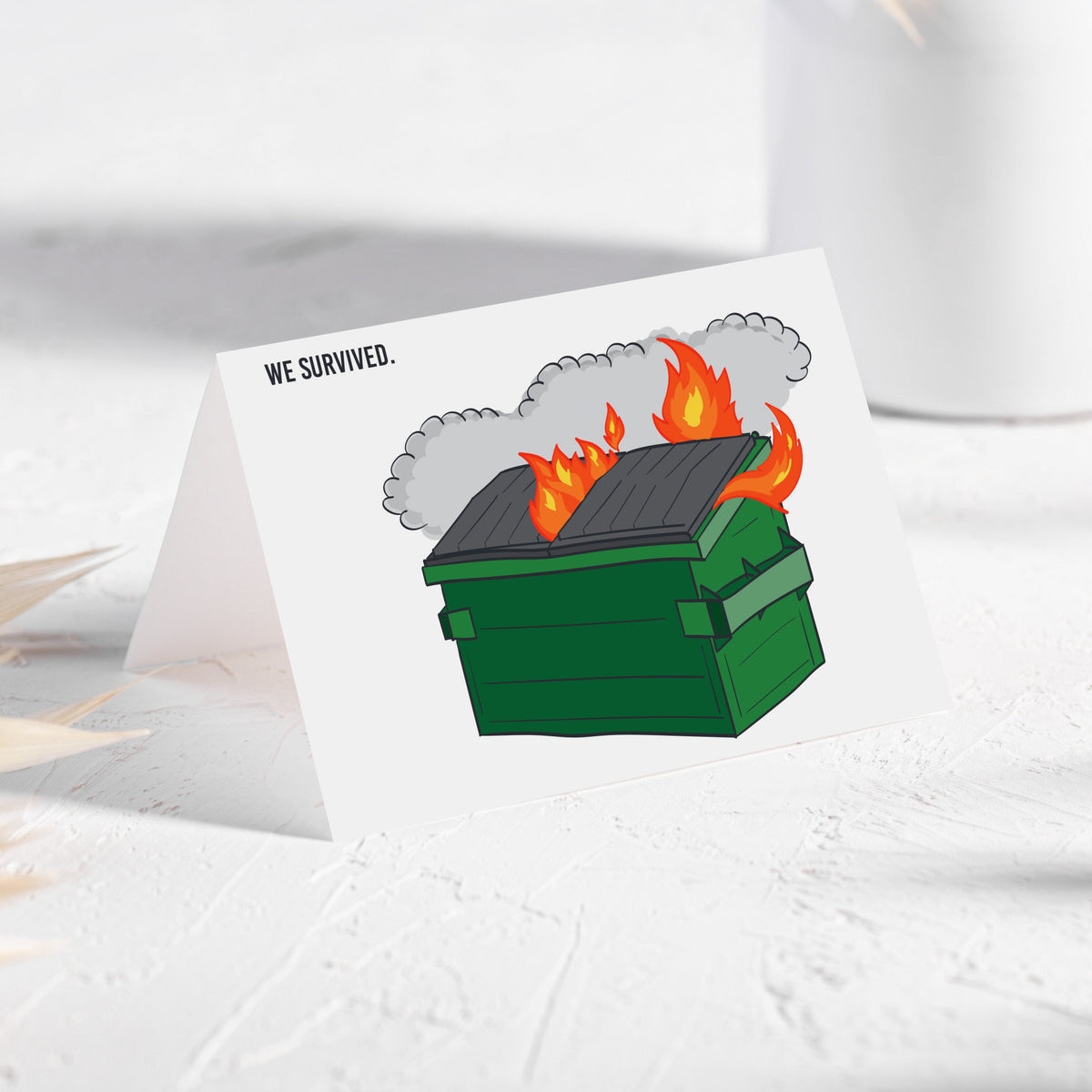 Card set featuring a forest green dumpster with orange and yellow flames and the words WE SURVIVED. on a white background.