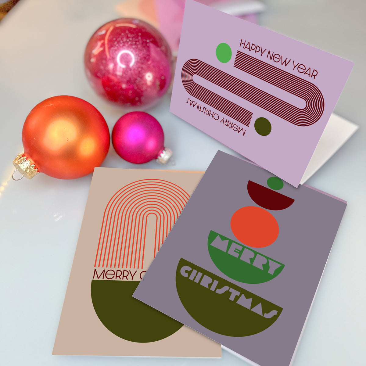 Holiday card set with flat geometric shapes and concentric line bands on solid lilac, tan, orchid, and gray-mauve backgrounds