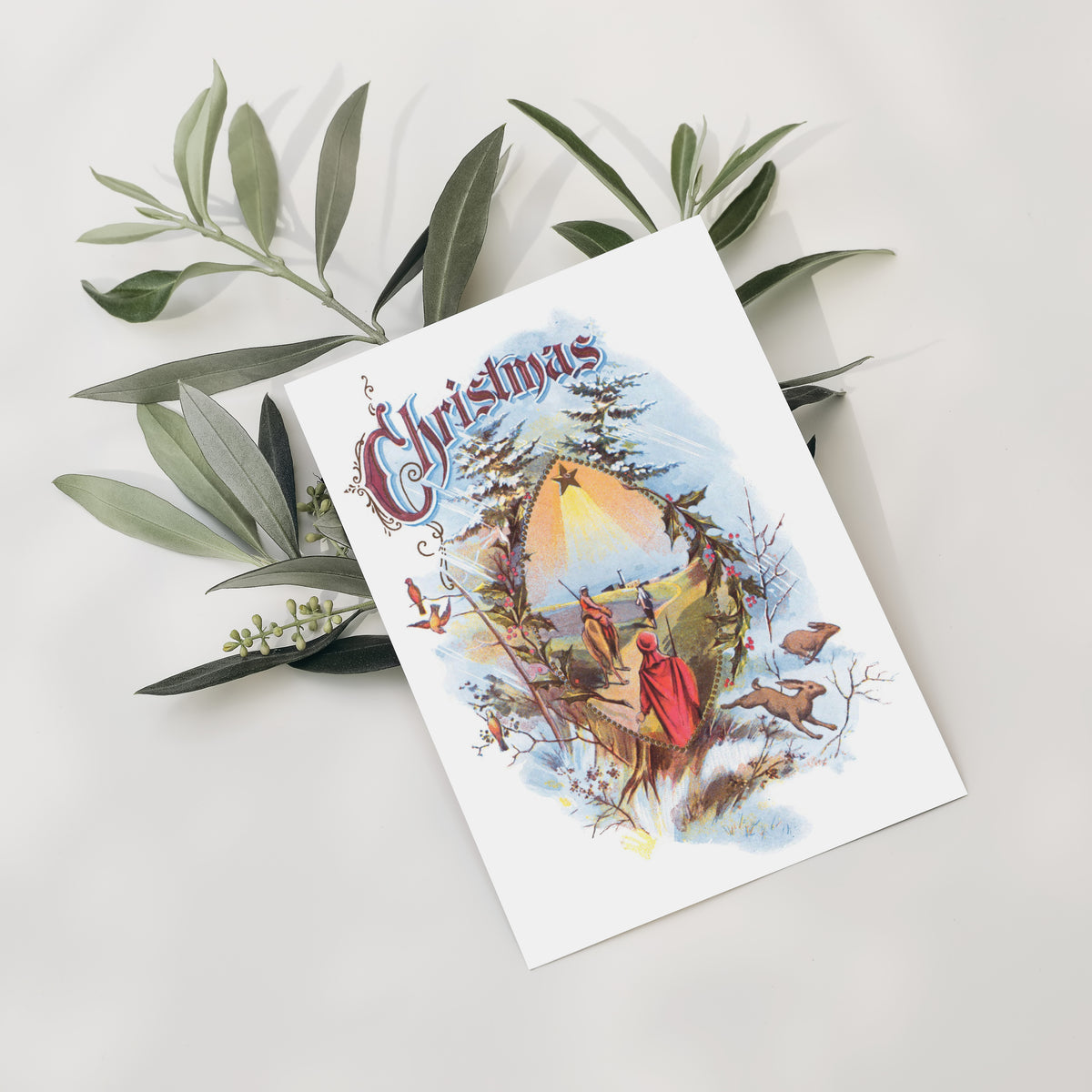 Victorian-style nativity card with ornate burgundy "Christmas" lettering, songbirds, hares, and a pointed-arch window scene.