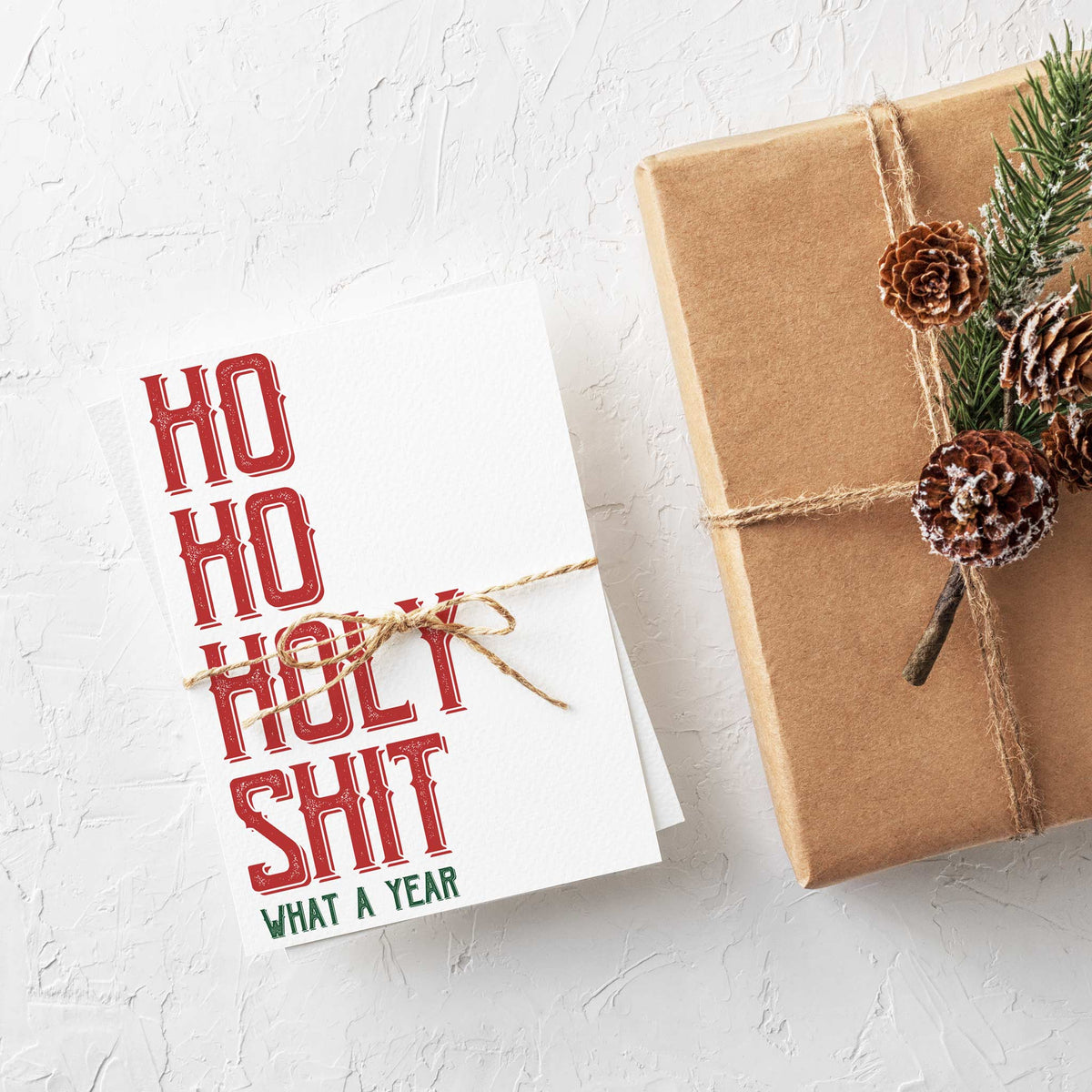 Repeated-design card front with stacked red serif text reading "Ho Ho Holy Shit" and smaller green "What A Year."