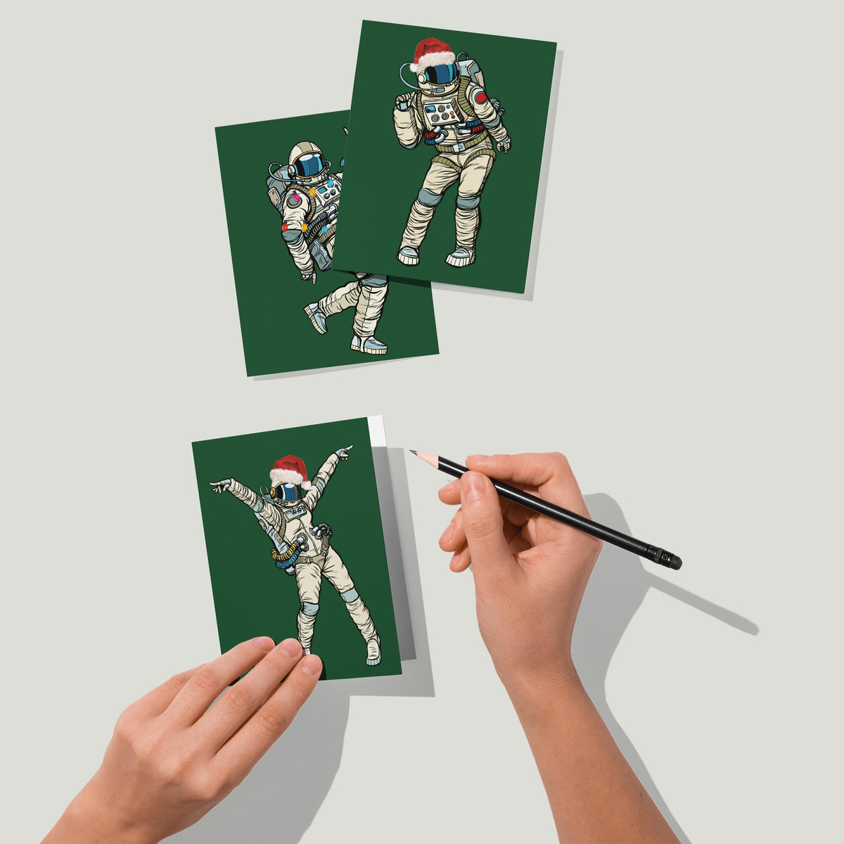 Four astronaut holiday card designs including Santa hats, string lights, antlers, and a striped scarf.