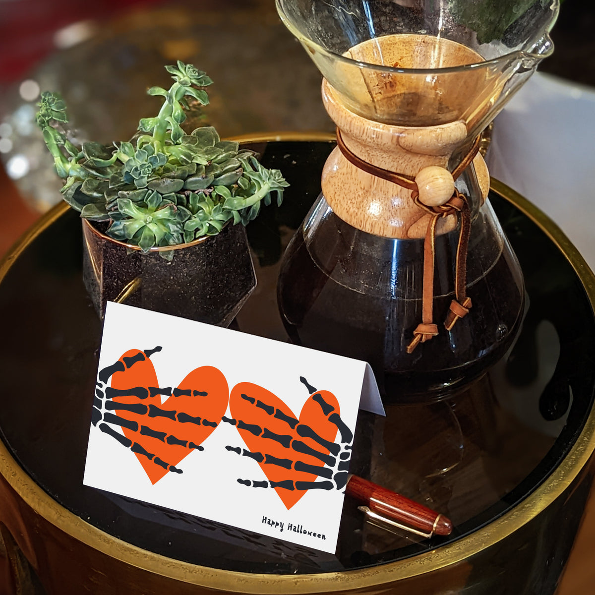 Halloween cards with a two-color graphic of skeleton hands and orange hearts, black script greeting.