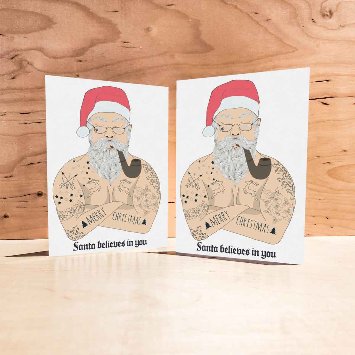 Christmas cards with a tattooed bare-chested Santa wearing round glasses and a red and white hat, pipe in mouth.