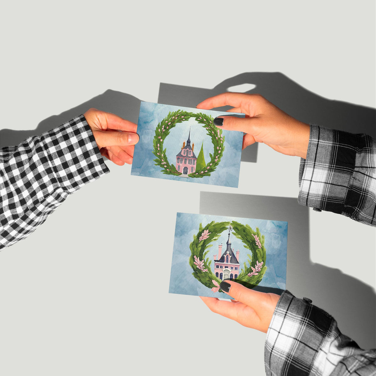 Christmas card set of 24 with a pink building, evergreen wreath, and blue watercolor-style sky on each design.