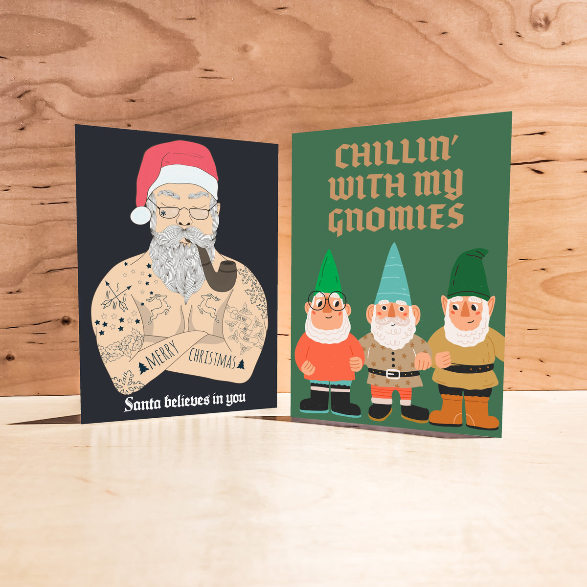 Holiday card pack with skeleton, gnome, and dinosaur designs on red, navy, black, and green backgrounds.