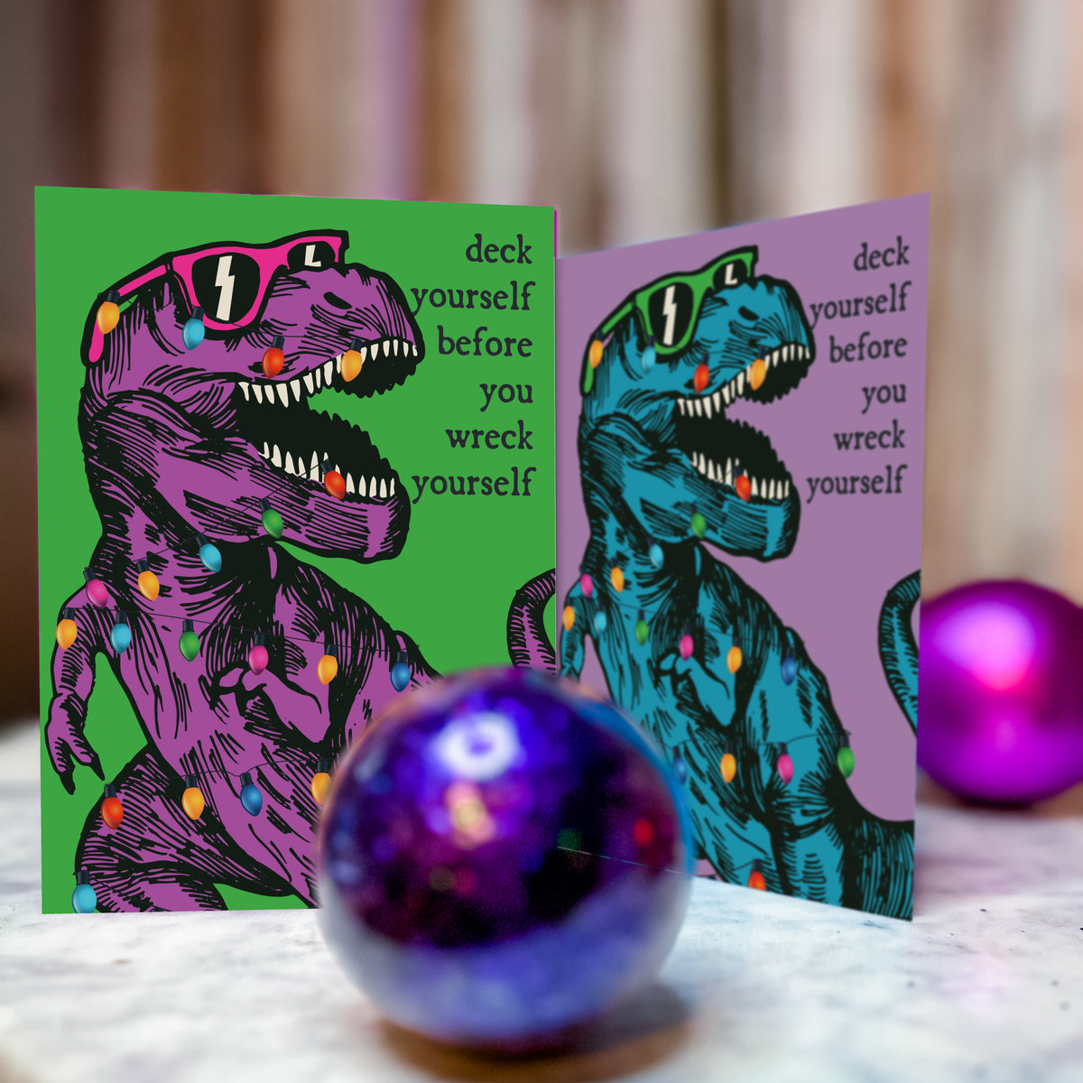 Portrait-format Christmas cards with a crosshatch-style dinosaur, hot pink or green sunglasses, C7 bulbs.