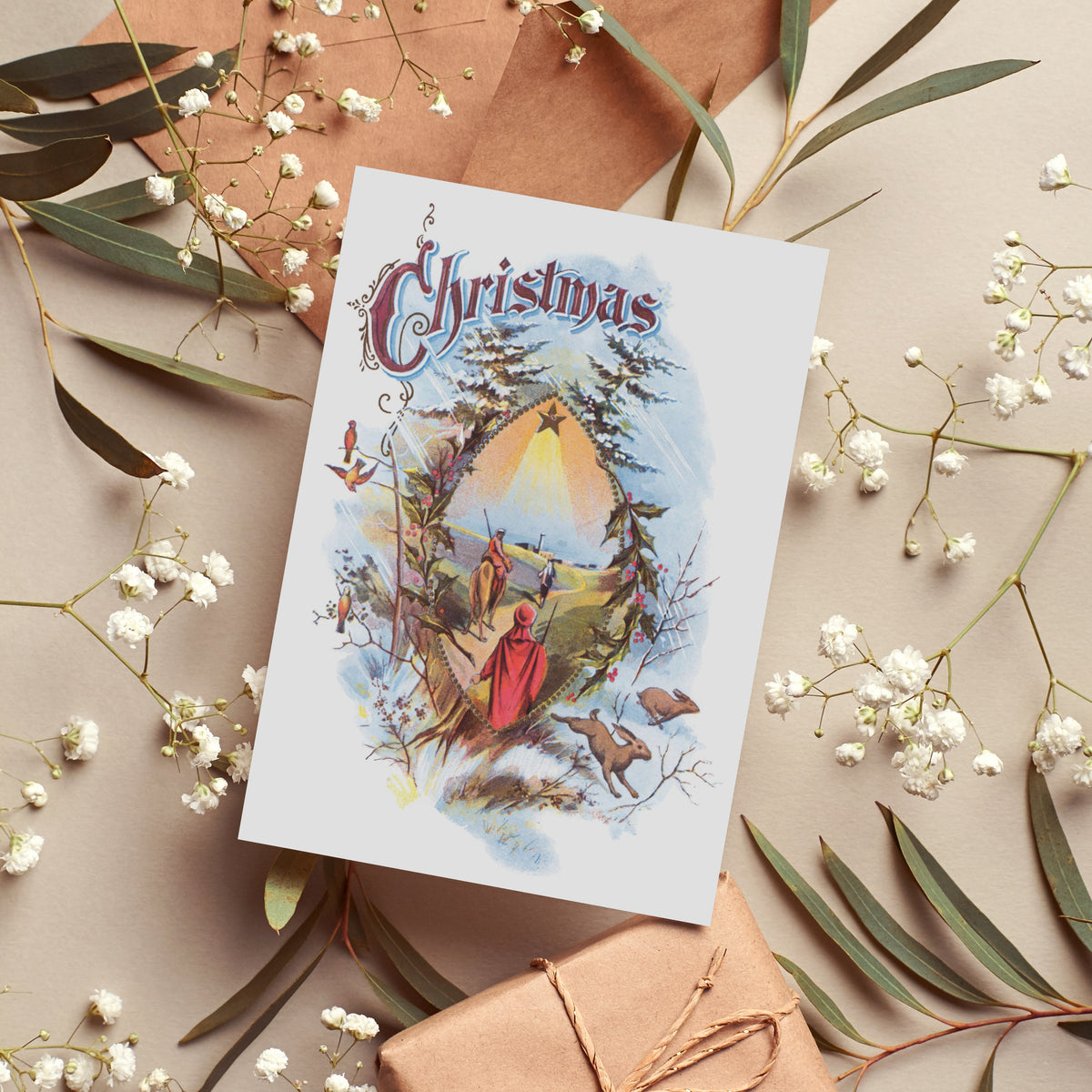 Christmas card set with one design: Magi, camel, holly border, snow-covered firs, and red-cloaked foreground figure.