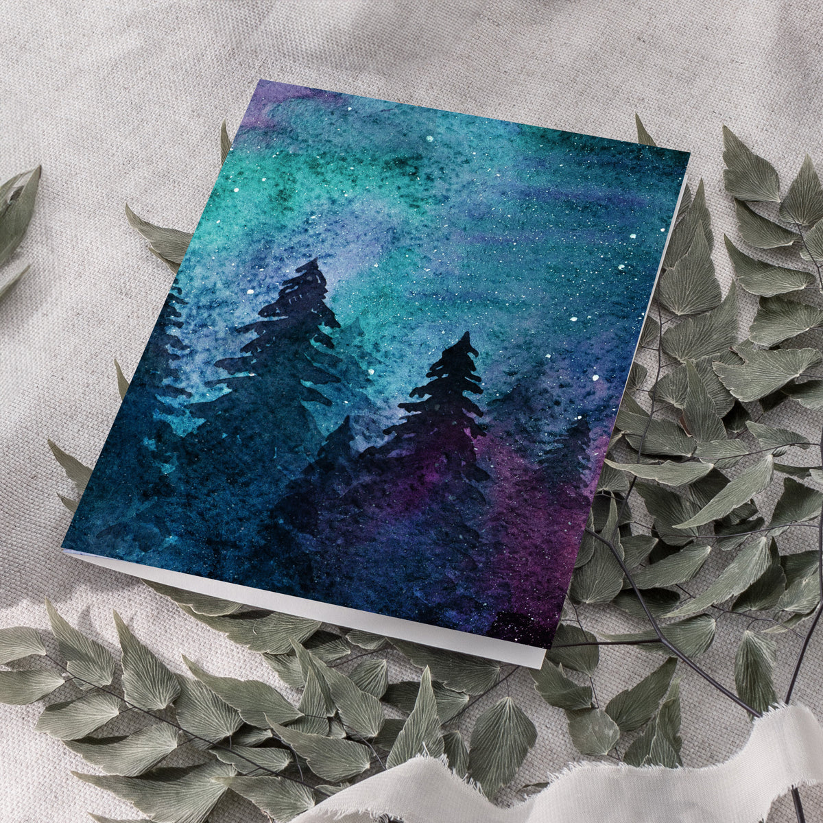 Watercolor sky card with scattered white dots and a black evergreen treeline along the bottom edge.