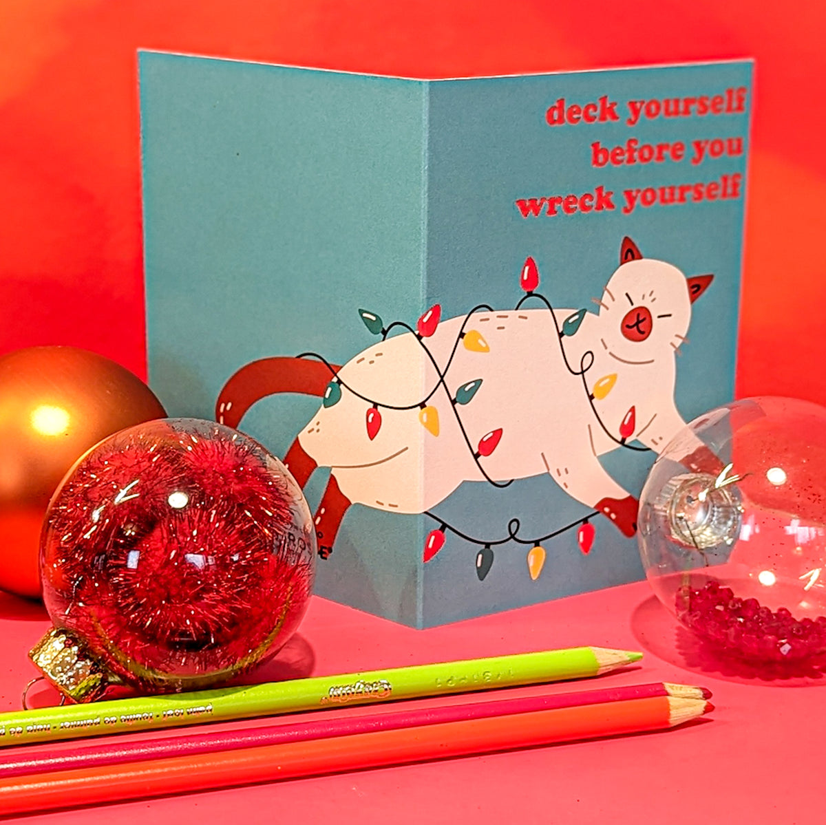 Christmas card collection showing illustrated cats paired with punny captions on bold color backgrounds.