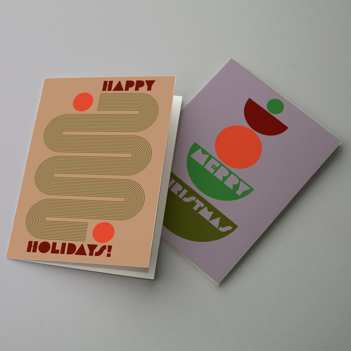 Geometric holiday cards with serpentine line bands, rainbow arches, stacked bowls, and circle accents in maroon, olive, and o