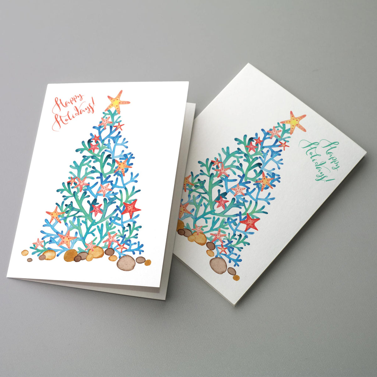 Christmas cards with a coastal theme, showing a coral-branch tree sitting on tan and brown beach stones.