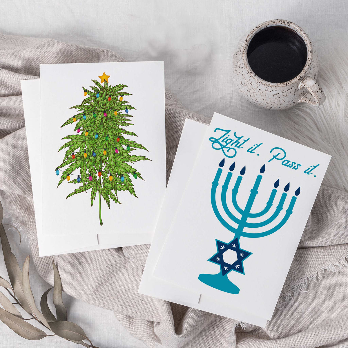 Cannabis holiday cards reading "Happy Holidaze," "Feliz NAVIDab," and "Get Lit," with envelopes.