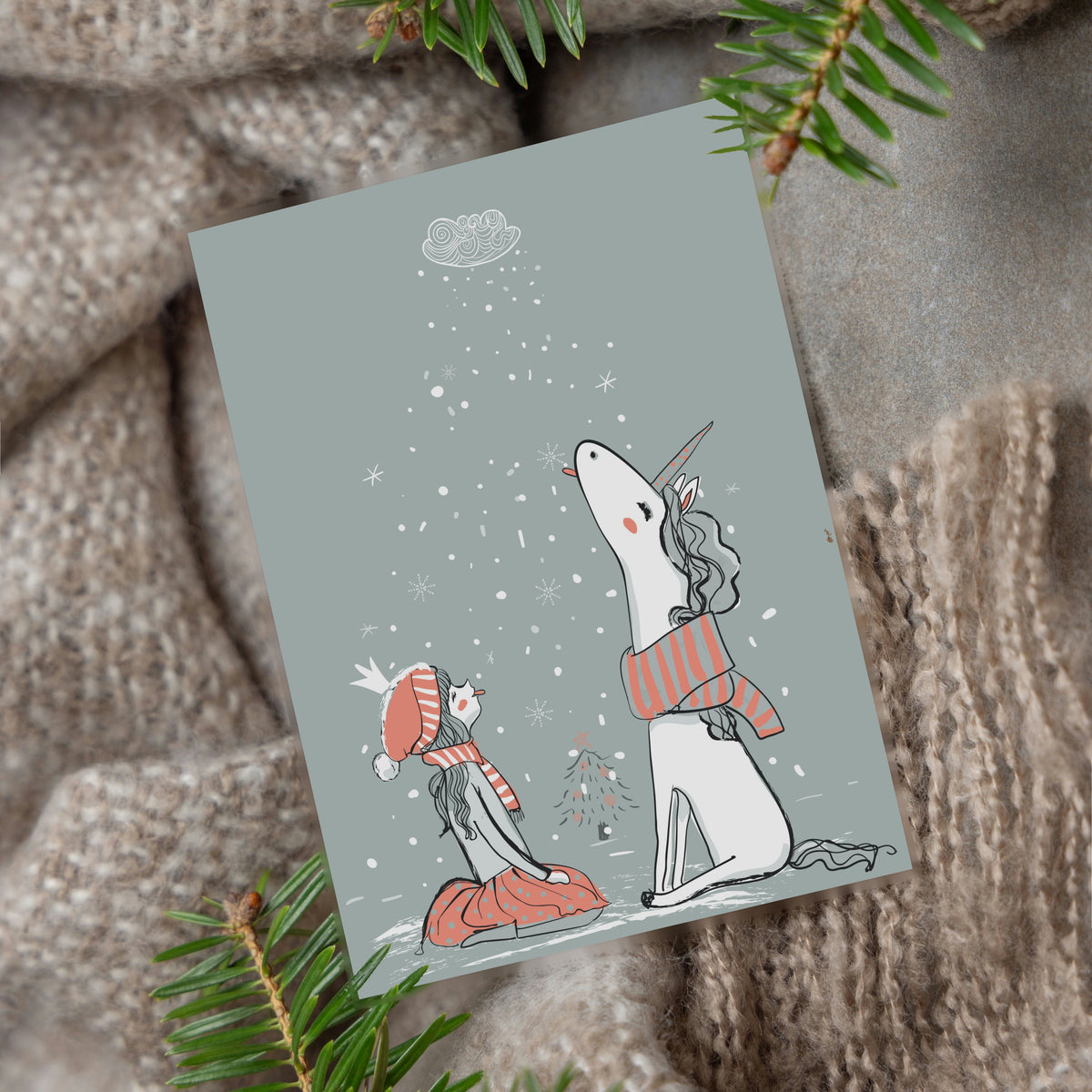 Gray background greeting cards with red and white striped accents on a girl and unicorn flanking a small Christmas tree.