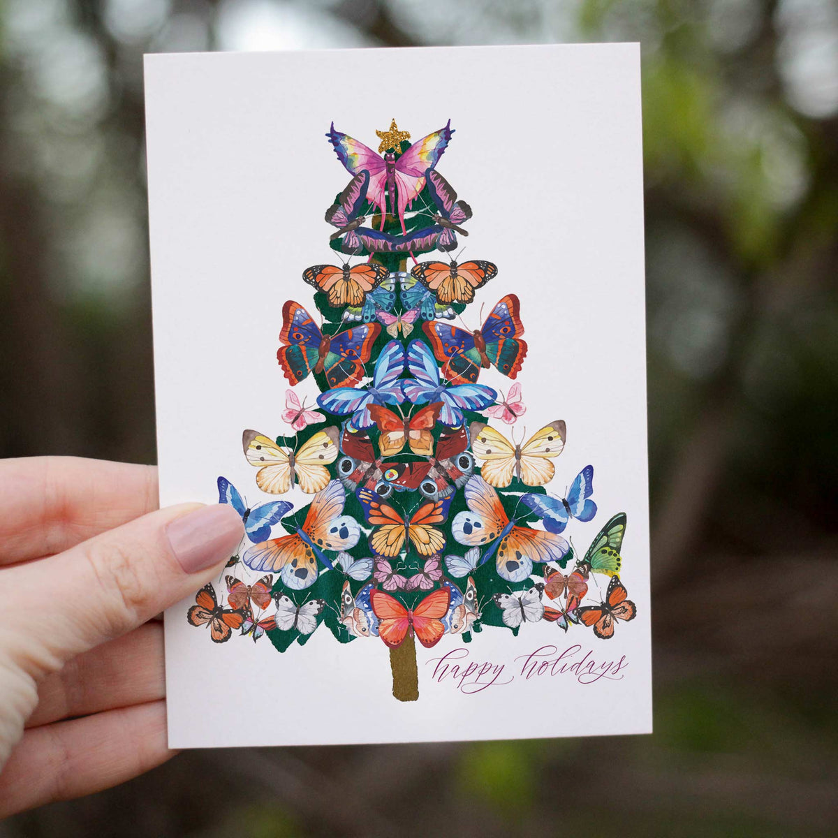 Christmas card depicting stacked tiers of patterned butterfly wings forming a tree shape with a fairy and star topper.