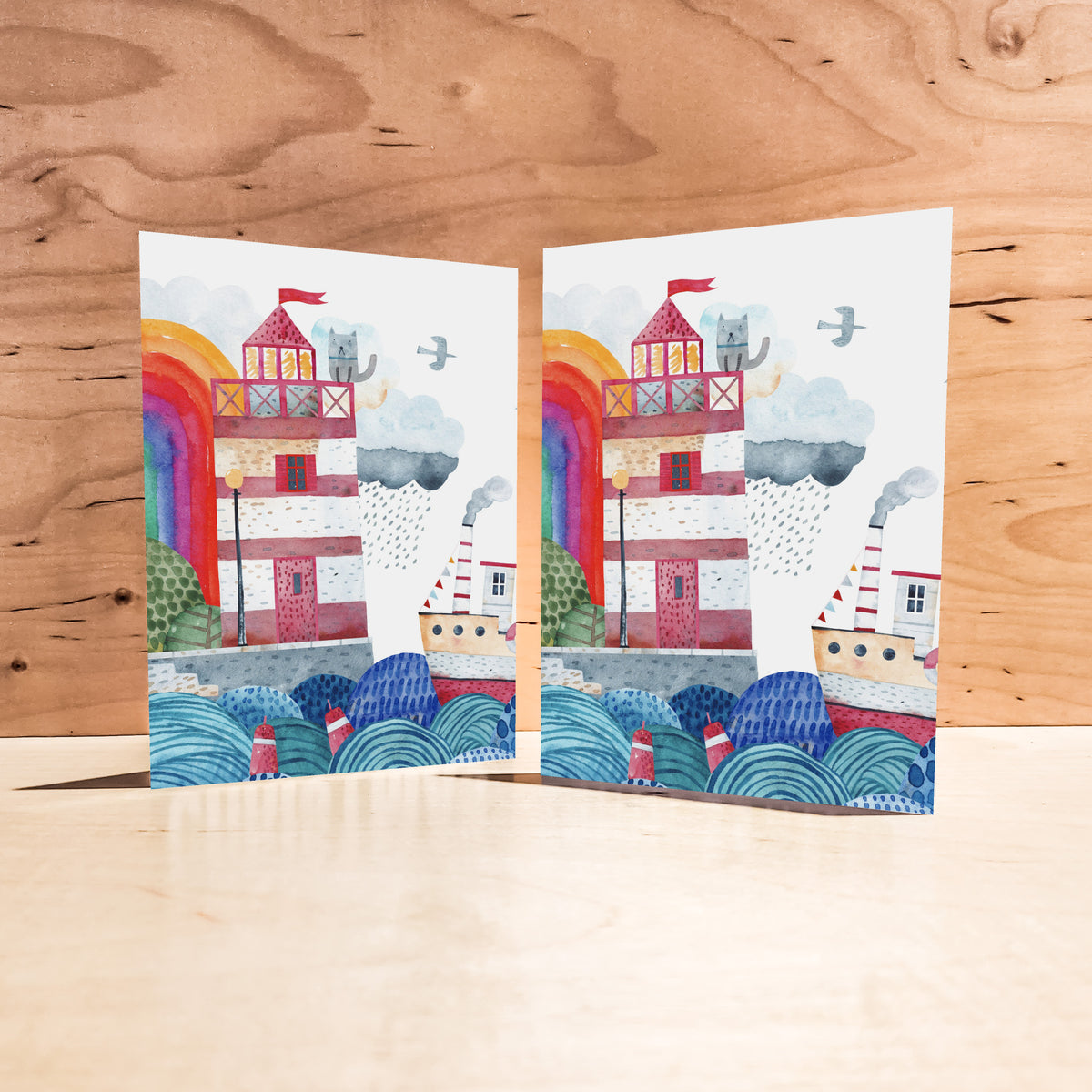 Boxed card set featuring a coastal scene with a rainbow arc, seagulls, rain cloud, and buoys.