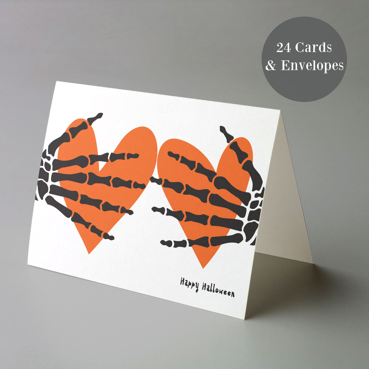 White greeting cards with centered orange heart and skeleton hand illustration, "Happy Halloween" text beneath.