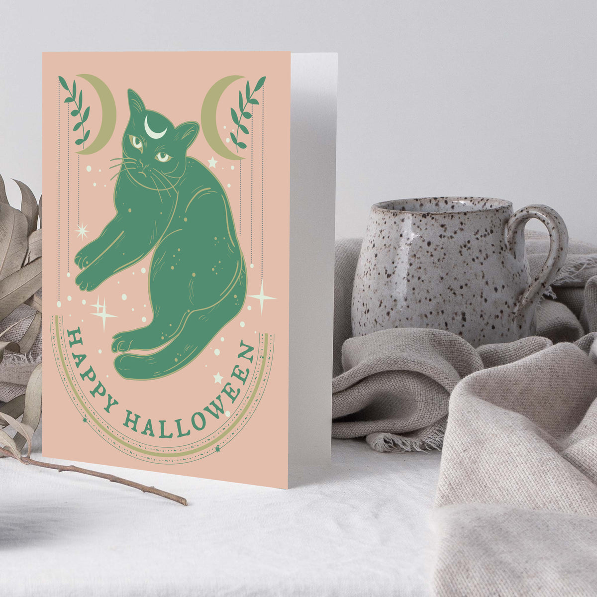 Green cat with crescent moon forehead mark on a muted peach Halloween notecard.