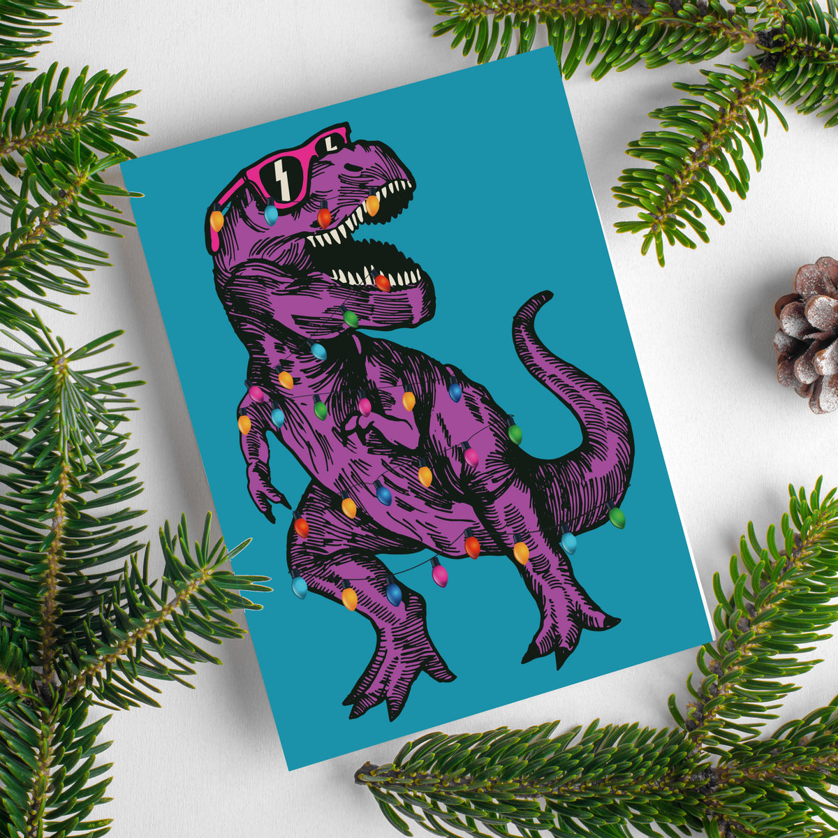 Holiday cards featuring a T-Rex wearing hot pink or turquoise sunglasses wrapped in multicolor Christmas bulbs.