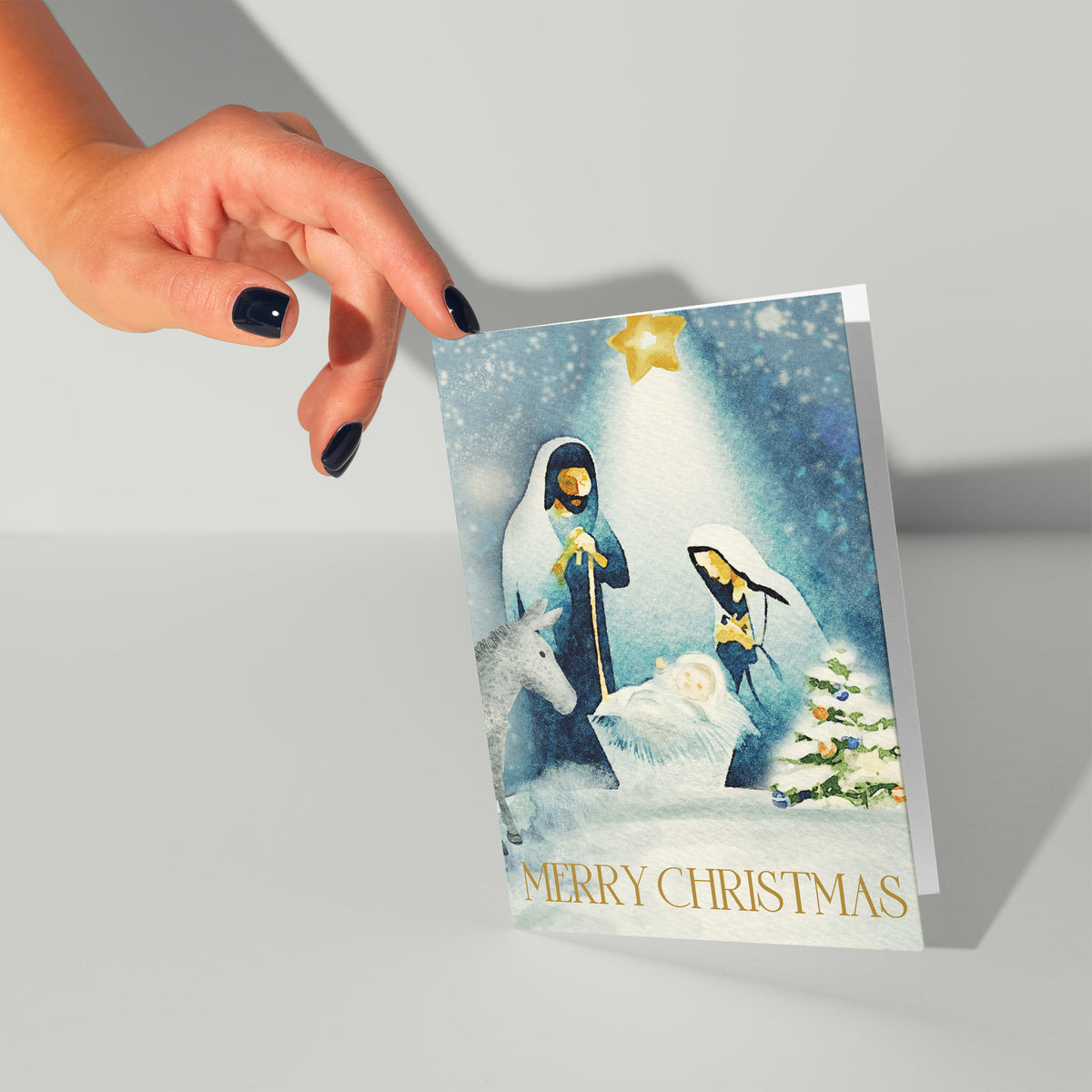 Watercolor Christmas card with nativity scene, white snow, gold "Merry Christmas" text in capital serif letters below.