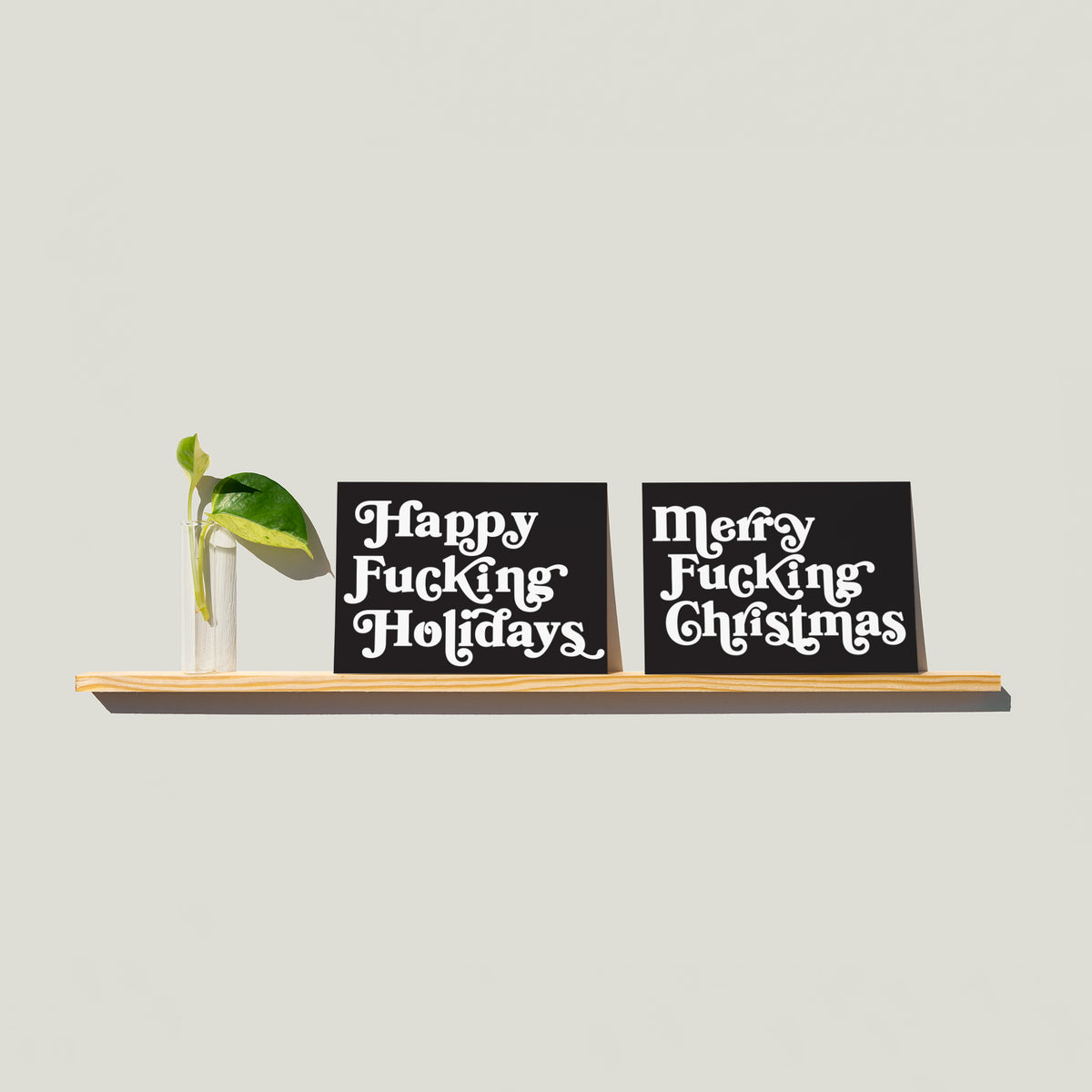 Christmas cards split across two designs, each with a single bold phrase in 1970s-style white serif type on charcoal.