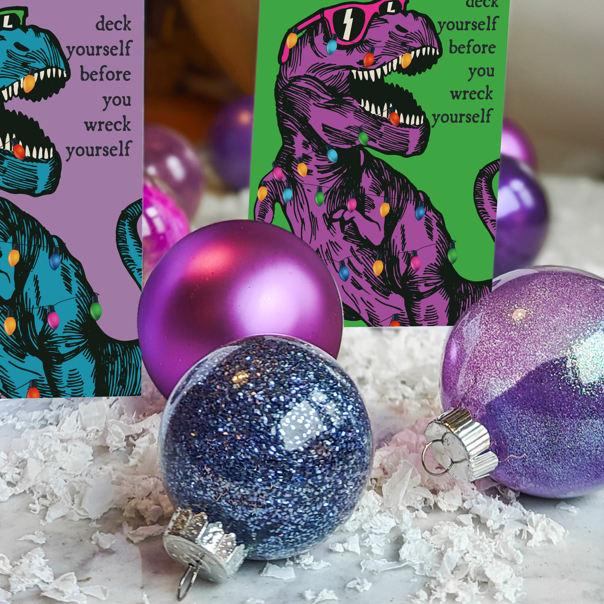 Christmas card pack with a purple-on-green and a teal-on-lavender dinosaur design, 12 cards per design.