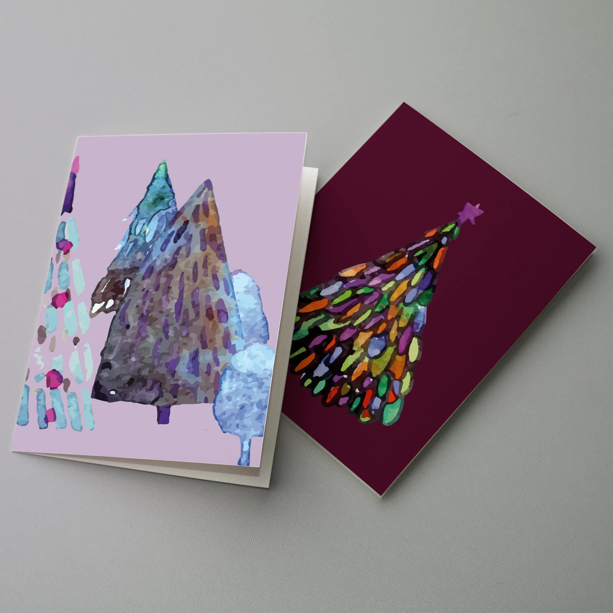 Holiday card pack with watercolor-style tree shapes in teal, navy, purple, cream, and green tones.