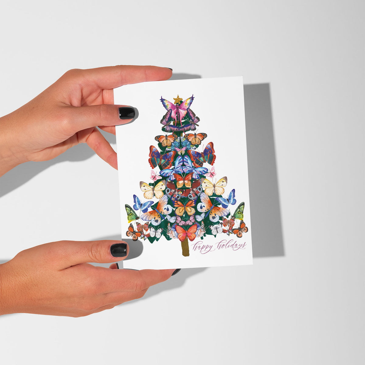 Pack of 24 identical Christmas cards with a butterfly tree design, fairy topper, and "Happy Holidays" in pink cursive script.