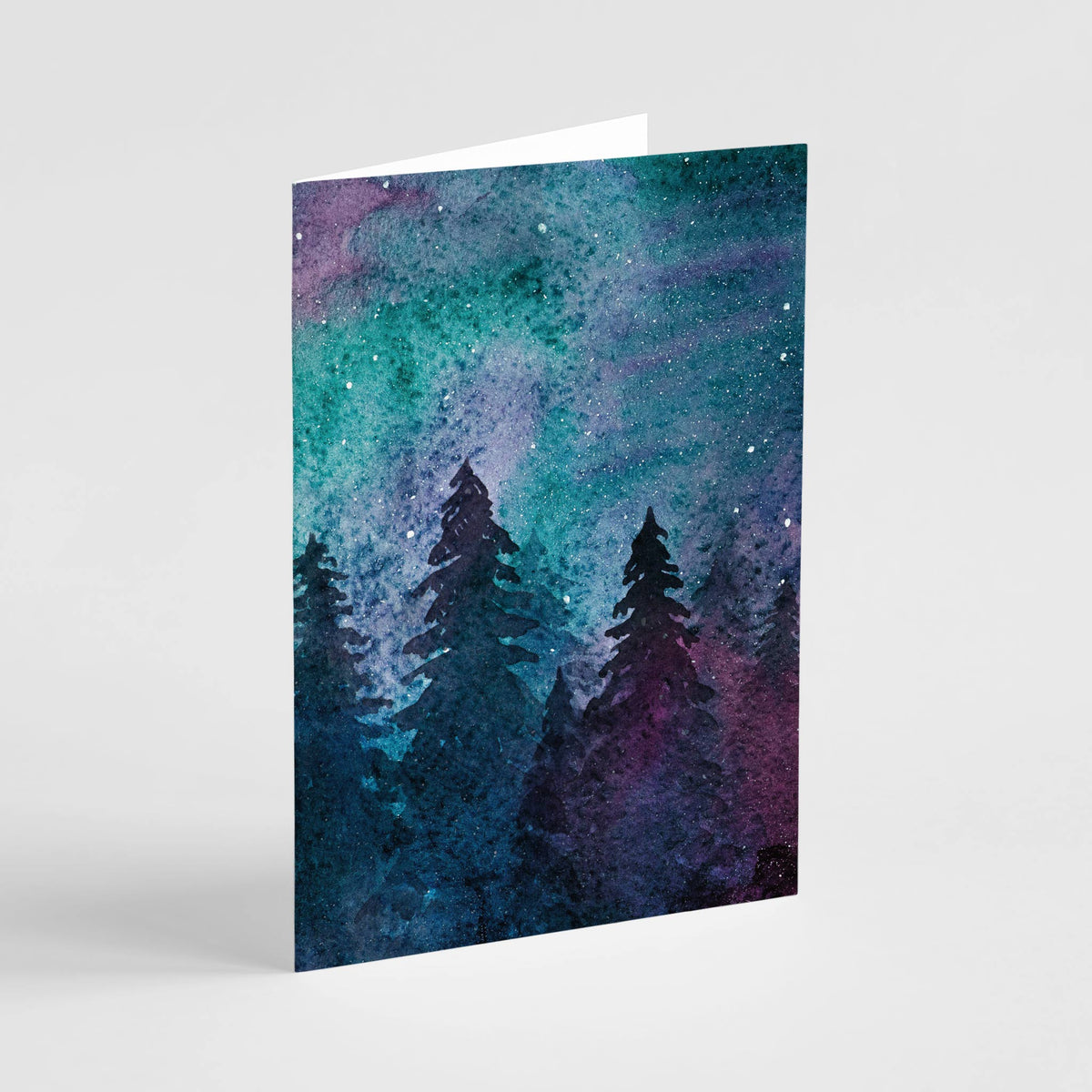 Set of 24 folded cards, one repeating design, watercolor sky in cool and warm tones above black silhouetted evergreens.