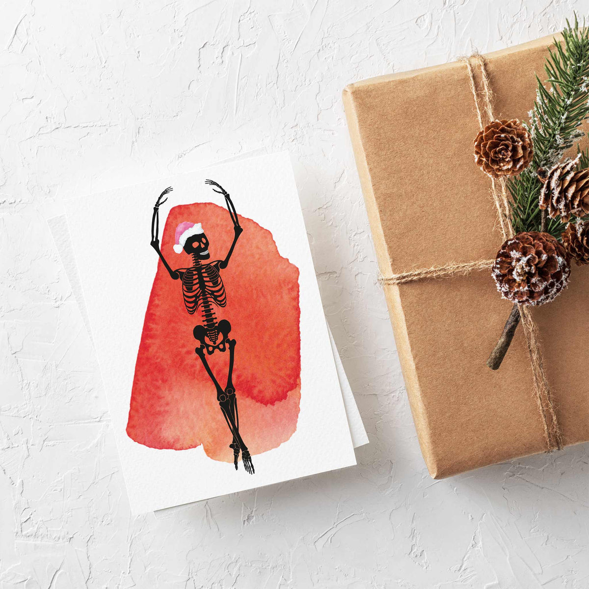 Black line skeleton figures in leaping ballet poses, each with a santa hat variant, on white cards with watercolor splashes.