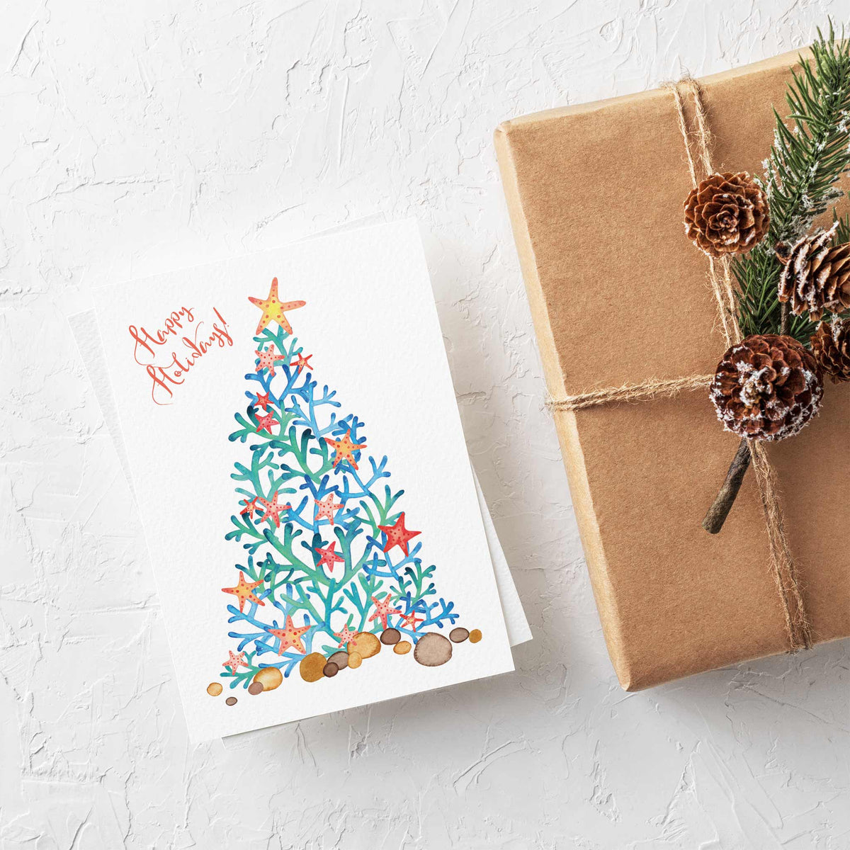 Holiday card pack with coral branch Christmas tree, starfish ornaments, and "Happy Holidays!" in brush-script lettering.