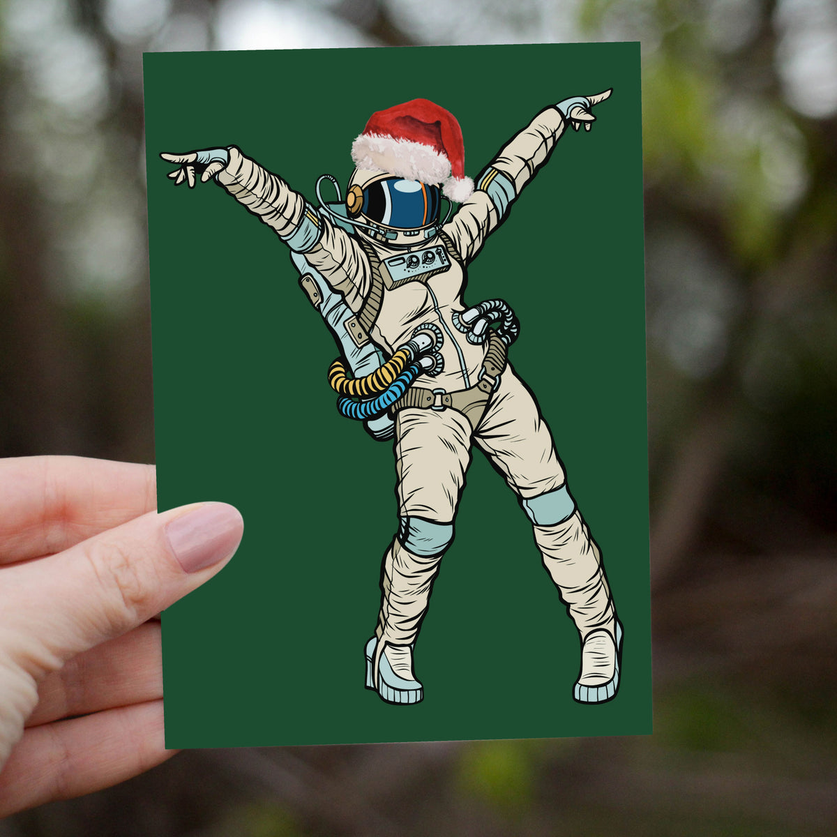 Astronaut wearing brown antlers and red-and-white striped scarf, one arm raised, dark green card.